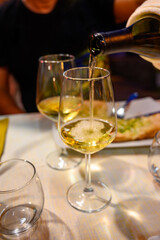 Pouring in glass  cold dry white wine in outdoor cafe at night in Italy