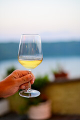 Hand with glass of cold dry white wine served outdoor in cafe at night in Italy