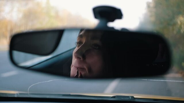 Woman paints her lips in the car mirrow