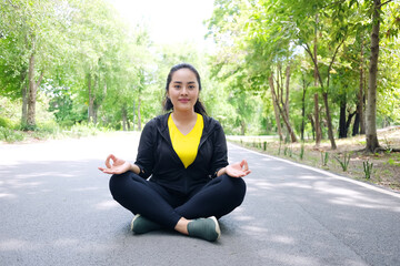 Obraz premium Smiling Asian young woman in sportwear sitting for yoga meditation for create concentration and calm the mind on wooden bridge after exercise in the natural light garden.