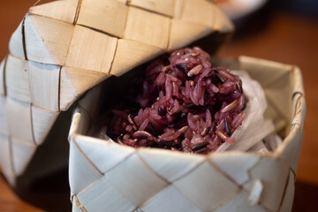 Black sticky rice in woven bamboo rice box on wood table.