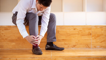 Close-up of an Asian man with leg pain due to twisted ankles while walking and holding on to sit.