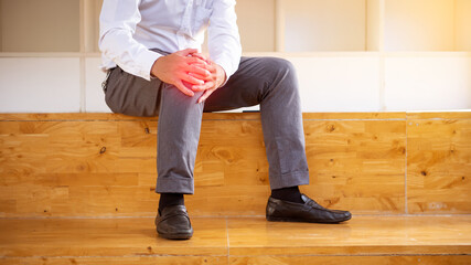 A man in work clothes has knee pain and is seated in his office.