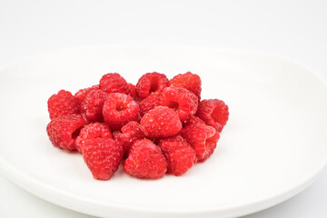 Fresh raspberries in small quantities are placed on a white plate on a light background. Berry background. The concept of proper nutrition