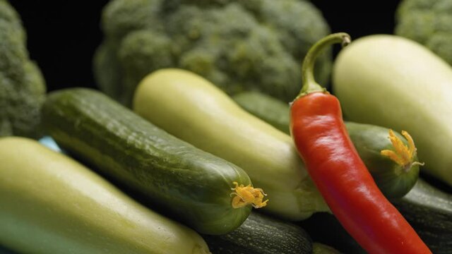 Close up fresh raw vegetables - zucchini, cabbage, broccoli and spicy pepper on the table on black background. Dolly shot