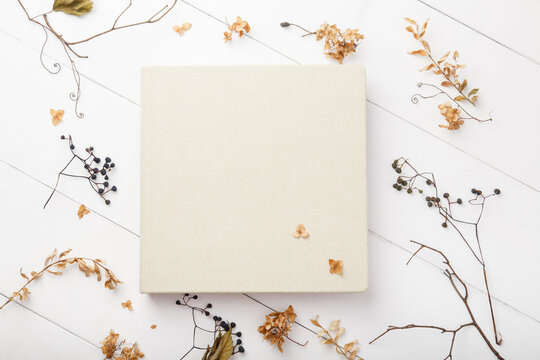 Elegant beige book with linen cover on white wooden background. Wedding photobook. Wedding photo album with autumn dried leaves and plants. School and autumn background. Fall mock up. Thanksgiving day