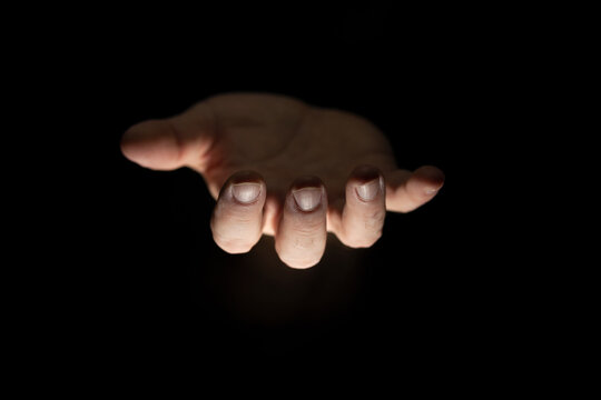 Male hand in the dark, palms facing upward, illuminated from  below, giving gesture