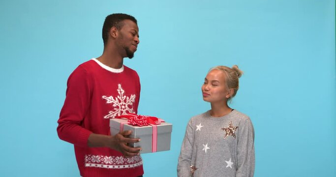 Studio, slow motion, man giving a Christmas present to an apprehensive woman