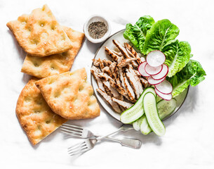 Mediterranean lunch - crispy italian focaccia, grilled turkey, green romaine salad and fresh vegetables on a light background, top view