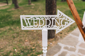White wooden sign in the form of an arrow and a pointer with the inscription and letters - wedding in English stands in nature at the ceremony. Photography, concept.