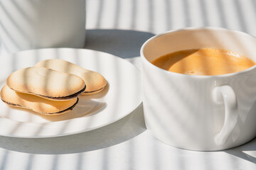 Cup of coffee and cookies close up on kitchen table in morning sunshine