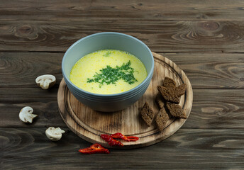 Cheese soup in a gray plate, with mushrooms, peppers and croutons on a wooden background.
