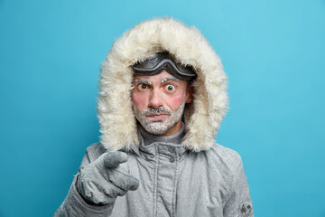 Displeased frozen man with red face points at camera in dissatisfaction blames you wears outerwear...