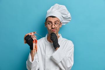 Photo of thoughtful male chef looks at crayfish and thinks what to cook for restaurant visitors...