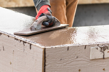 Construction Worker Using Wood Trowel On Wet Cement Forming Coping Around New Pool
