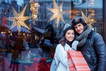 Obraz na płótnie Canvas Young couple doing christmas shopping in the city, smiling, embracing.