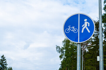 Blue sign on the pole of a pedestrian and Bicycle path against the background of blue sky and tree leaves.