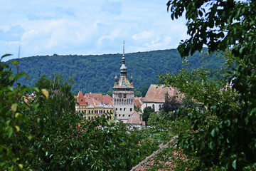 La torre del reloj de Sighisoara también conocida como la torre del consejo en Sighisoara, Rumania. Vista de la torre entre el follaje de los árboles y los tejados de la ciudad.