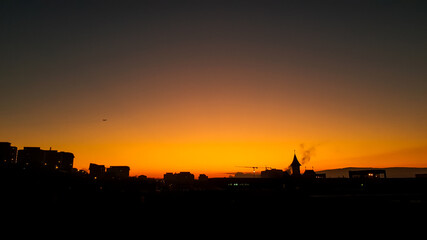 Sunrise with clear sky and plane and backlit city landscape