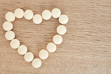 Fototapeta na wymiar White heart shape made from pills for therapy, concept of treatment and health care on wooden background. Medical banner, copy space