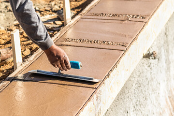 Construction Worker Using Trowel On Wet Cement Forming Coping Around New Pool
