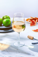 Still life of a large glass of white wine and a plate of green apples in the sunlight.