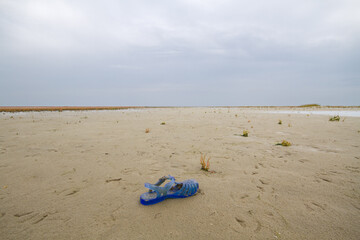 Fototapeta na wymiar Blue plastic children’s sandal washed up the beach