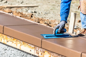 Construction Worker Using Trowel On Wet Cement Forming Coping Around New Pool