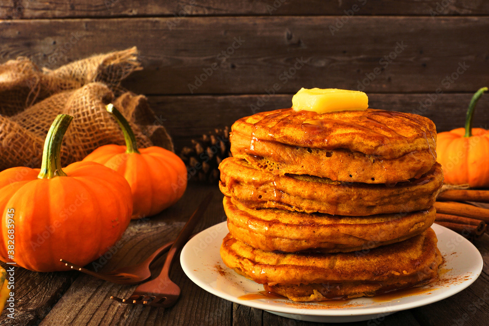 Poster stack of pumpkin spice pancakes with caramel sauce. side view table scene on a dark wood background.