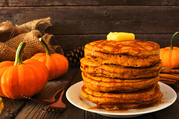 Stack of pumpkin spice pancakes with caramel sauce. Side view table scene on a dark wood...