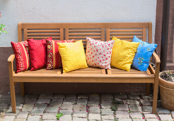 Wood bench outside with much multicolor pillows.