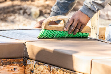 Construction Worker Using Brush On Wet Cement Forming Coping Around New Pool