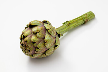 Two organic artichokes with a piece of stem on a white surface.