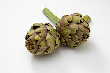 Fototapeta premium Two organic artichokes with a piece of stem on a white surface.