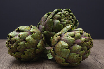 Obraz premium Close up of Three fresh organic purple artichokes with stem on a rustic wooden surface and dark background