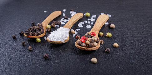 Salt and whole black peppercorns, pepper mix in wooden spoons, top view