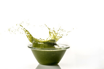Genoese pesto splashes out of a clear glass bowl, still