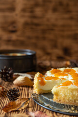 Cheesecake oder Käsekuchen mit fruchtigen orangen Mandarinen auf einem Tisch aus Holz im Herbst mit Laubblättern