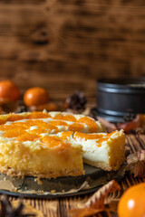 Cheesecake oder Käsekuchen mit fruchtigen orangen Mandarinen auf einem Tisch aus Holz im Herbst mit Laubblättern