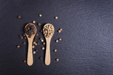 Black and whole white peppercorns, pepper mix in wooden spoons, top view