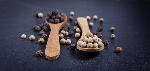 Black and whole white peppercorns, pepper mix in wooden spoons