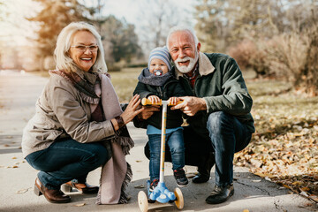 Happy good looking senior couple husband and wife walking and playing with their adorable grandson...