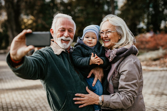Happy good looking senior couple husband and wife walking and playing with their adorable grandson in public city park