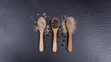 Black whole peppercorns and pepper powder, pepper mix in wooden spoons