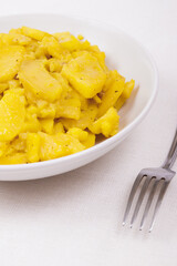 Stewed potato with spices in bowl with silver fork on the tablecloth.