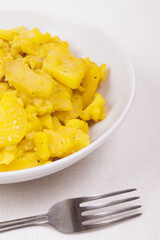 Stewed potato with spices in bowl with silver fork on the tablecloth.