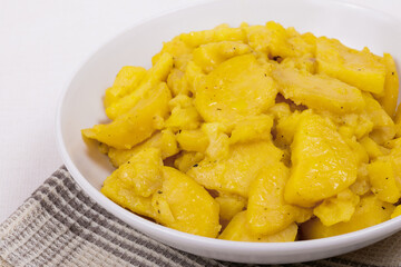 Stewed potato with spices in bowl on checkered napkin.