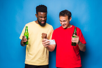 Two mixed race men drink beer look at phone isolated on blue background