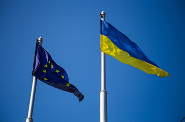 European union flag and ukrainian flag fluttering against blue sky background