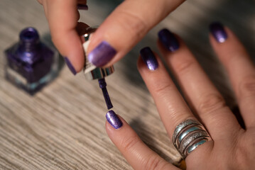 The woman is painting her nails purple, close up